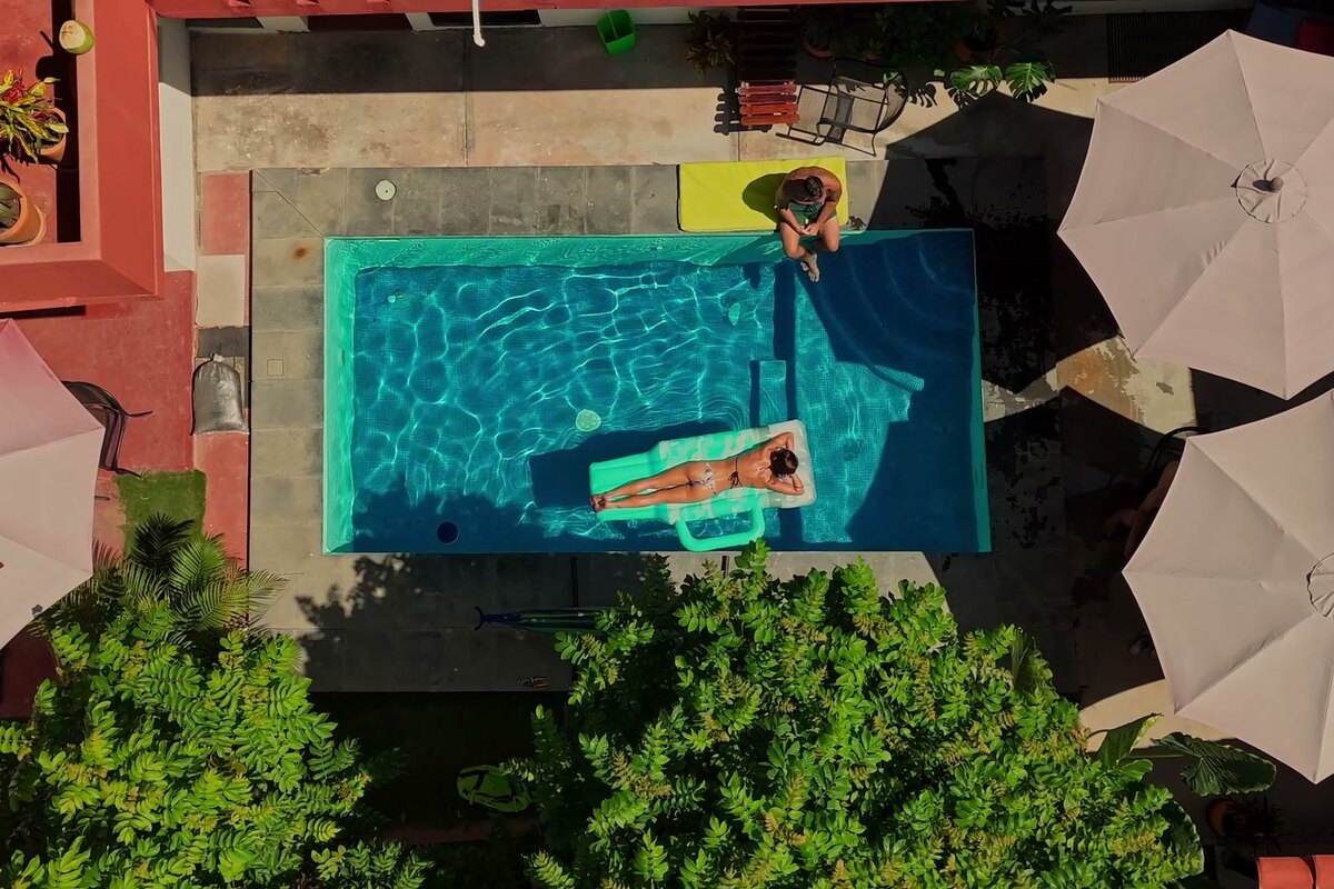 Looking straight down on the courtyard pool — turquoise water, a float, sun umbrellas, and greenery all around