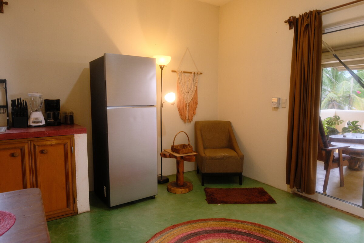 Casa Bel living area — armchair and full-size fridge beside sliding doors that open to the private terrace