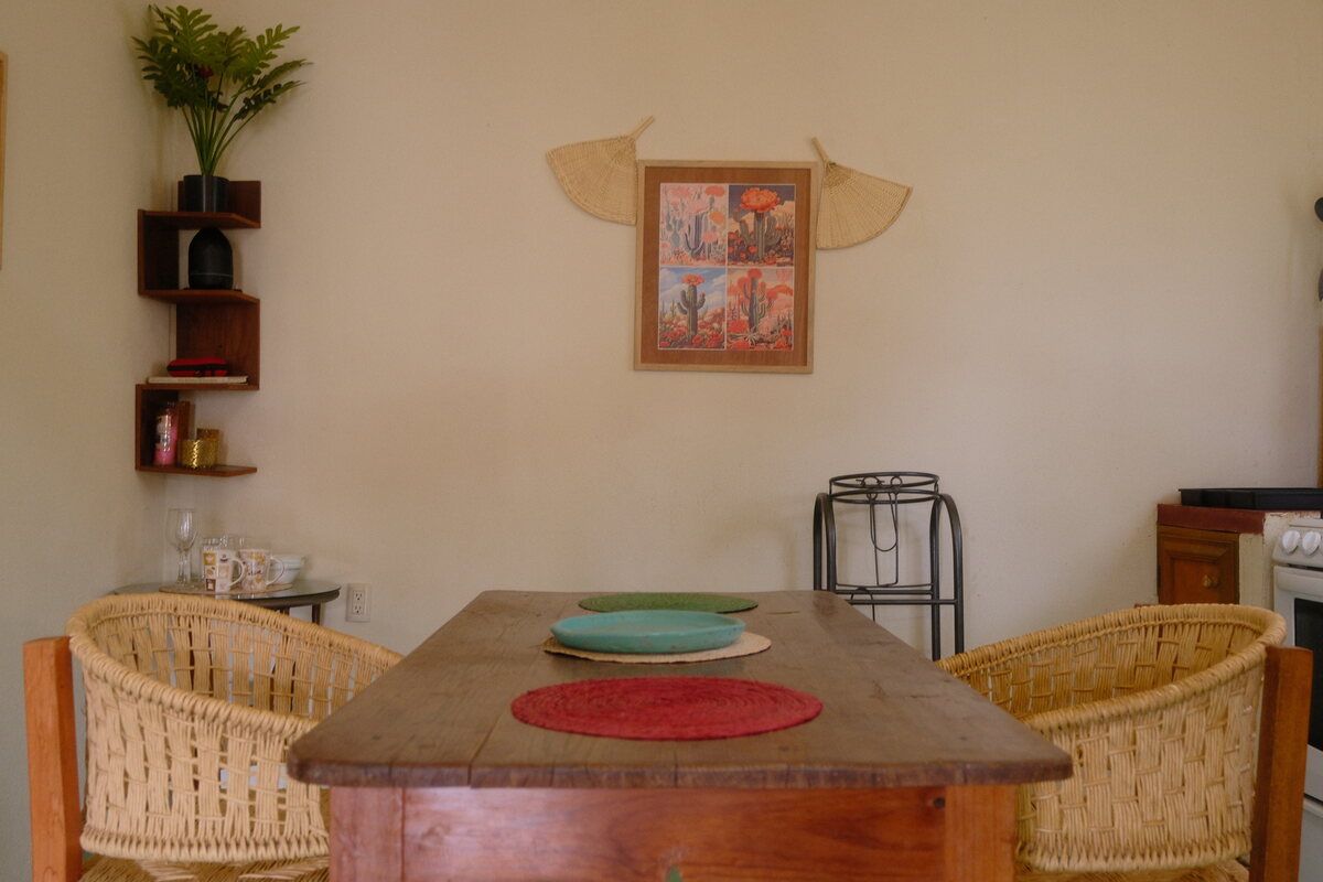 Casa Bel dining table — solid wood table with woven chairs beneath a folk-art print