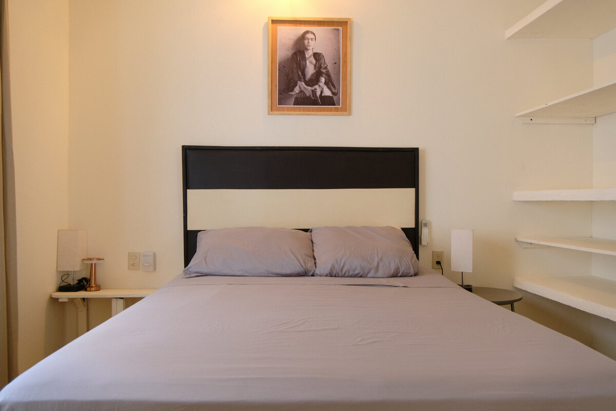 Casa Linda bedroom — bed with a framed portrait and open shelving