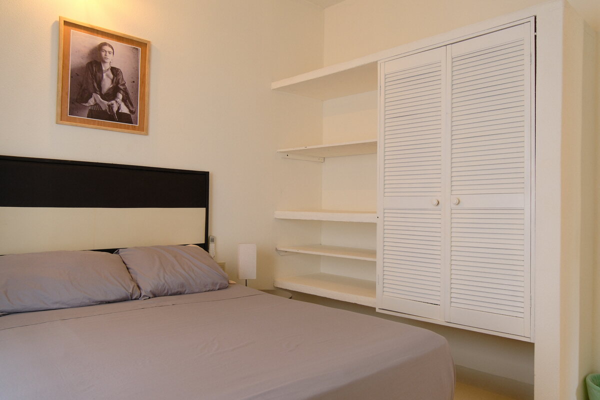 Casa Linda bedroom — bed beside a louvered wardrobe and built-in shelves