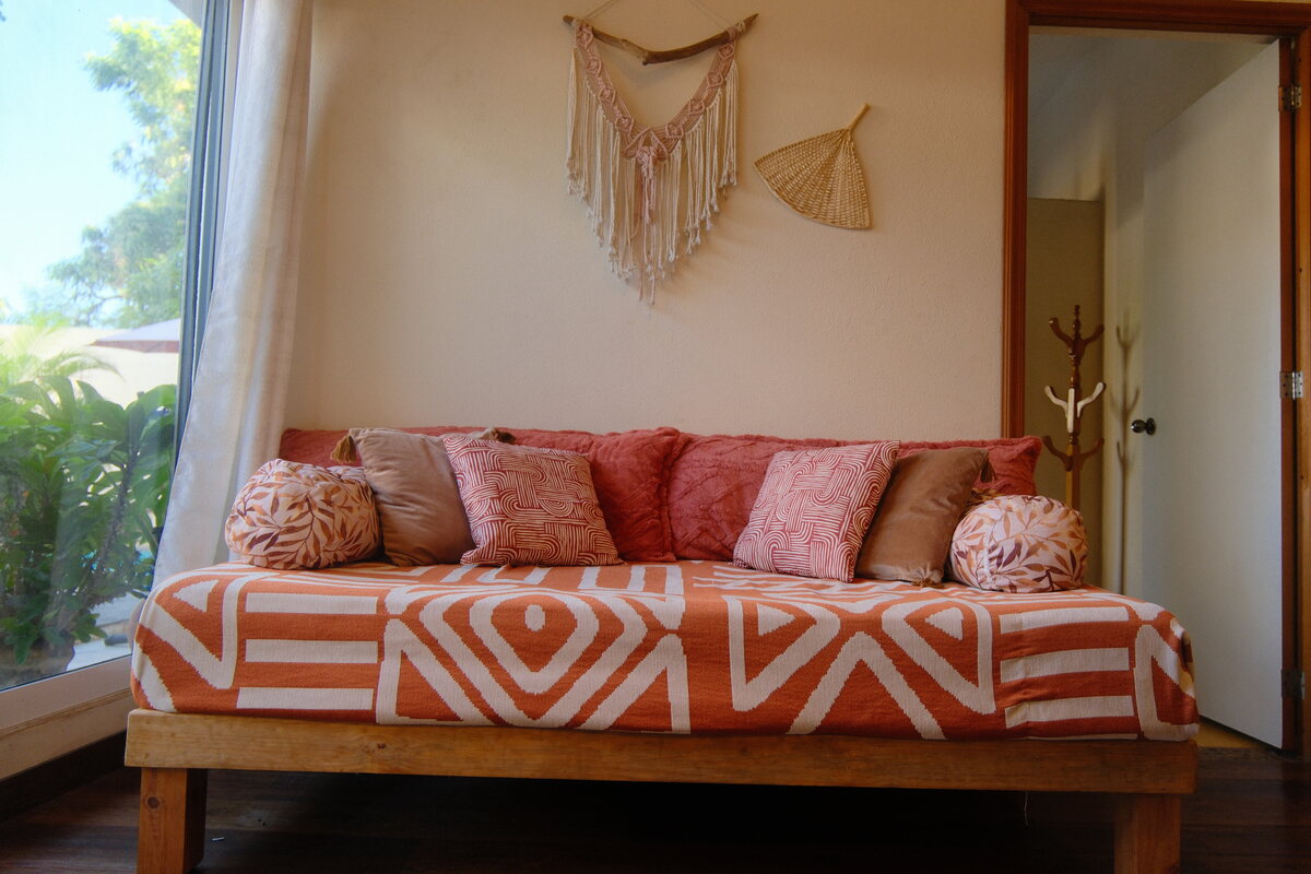 Casa Mia lounge — patterned sofa with pillows beneath a macramé wall hanging