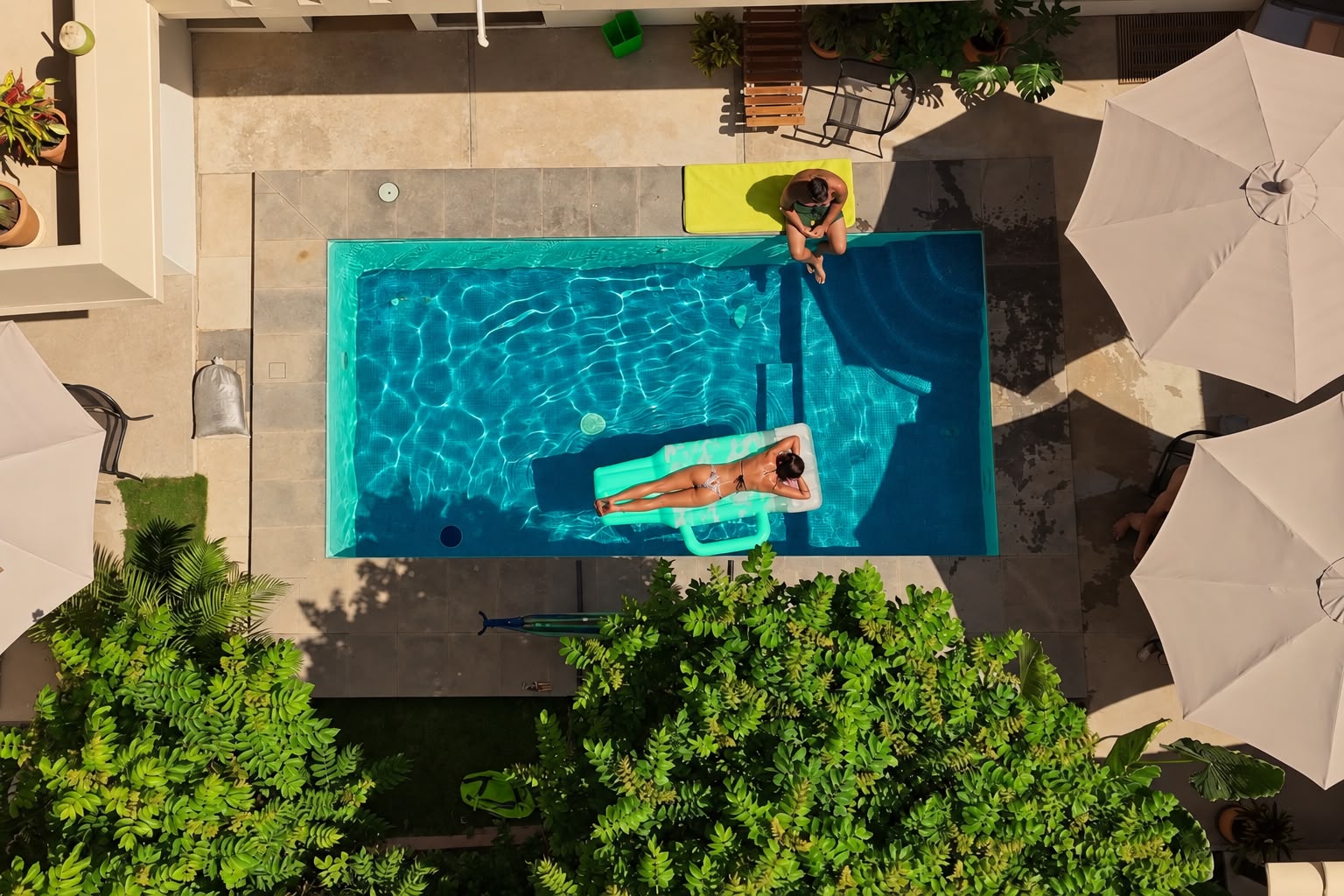 Looking straight down on the courtyard pool — turquoise water, a float, sun umbrellas, and greenery all around